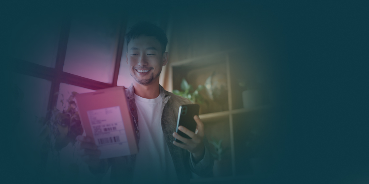 Leende person tar emot ett paket vid dörren medan hen håller en mobiltelefon